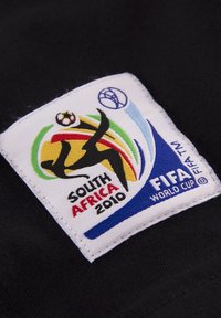 Witte stoffen patch met een kleurrijk FIFA Wereldbeker logo, met zwarte, gele, groene en blauwe elementen, genaaid op een zwart kledingstuk.