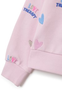 Sudadera rosa con texto bordado "LOVE THERAPY" y corazones coloridos en azul, rosa y plateado. Presenta puños acanalados y una textura suave.