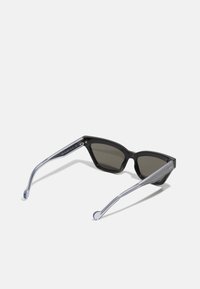 Occhiali da sole neri angolari con lenti scure, aste trasparenti con motivo e dettagli argentati alla tempia, caratterizzati da un design elegante e moderno.