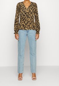 Blusa con stampa giaguaro, scollo a V, maniche lunghe e vita arricciata, abbinata a jeans a gamba dritta di colore azzurro chiaro e tacchi con cinturini.