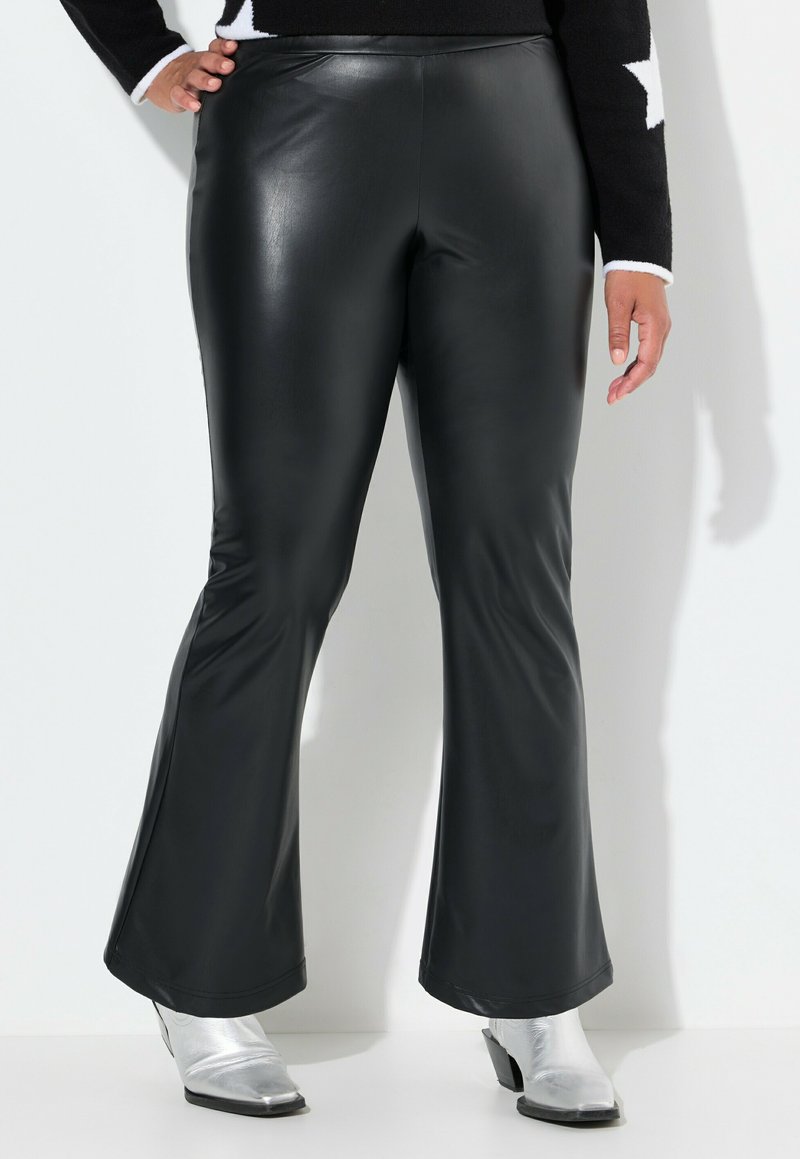 Pantalons évasés en faux cuir noir avec une texture lisse et une coupe slim au niveau des cuisses, présentant un ourlet large au bas. Bottines argentées visibles.