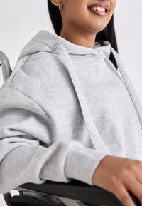 Lys grå hettegenser med en avslappet passform, som har en stor hette og snorer. Glatt tekstur, synlig søm og ribbestrikkede mansjetter.