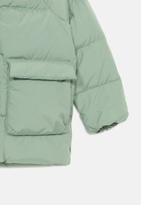 Polstret jakke i lys grønn, med en frontlomme, samlede ermer og en glatt, blank overflate.