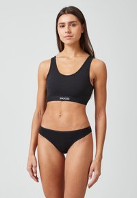 Czarny bawełniany biustonosz typu braletka z szerokimi ramiączkami i elastycznym paskiem z logo. Pasujące czarne majtki bikini o niskim stanie i minimalnym kryciu. Gładka tekstura.