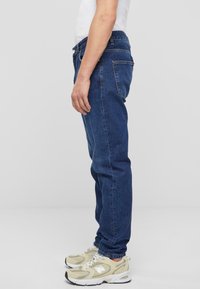 Jeans de mezclilla azules con corte recto, cinco bolsillos y cierre de botón. Combinados con zapatillas deportivas beige con detalles en gris.