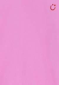 T-shirt rose en tissu lisse avec un petit visage souriant orange brodé sur le côté supérieur gauche. Design simple, coupe décontractée.