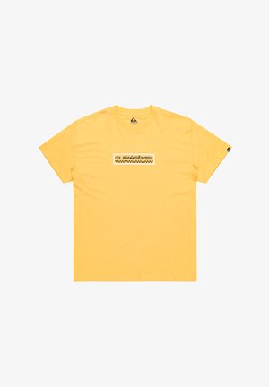 Keltainen puuvillapaita, jossa on suorakulmainen musta logo, jossa on ruudullinen kuvio keskellä. Lyhyet hihat, ymp roundkauluksella.