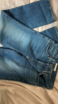 Jean en denim bleu avec une finition délavée, coupe droite, design à cinq poches et détails de couture. Une paire est superposée sur l'autre.