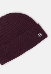 Berretto lavorato a maglia color bordeaux con texture a coste e risvolto, caratterizzato da un accento di logo metallico circolare.