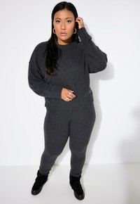 Suéter de punto gris y leggings a juego, con un corte relajado, puños acanalados y una textura suave. Llevado con calzado negro con cordones.