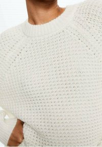White knitted sweater featuring a textured pattern, round neckline, and raglan sleeves. The fabric appears soft and loosely woven.