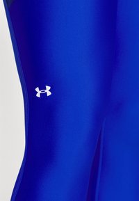 Niebieskie sportowe legginsy wykonane z gładkiej tkaniny, z białym logo Under Armour na lewej udzie i smukłym designem.