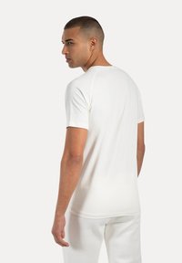 Weißes Baumwoll-T-Shirt mit kurzen Ärmeln, rundem Ausschnitt und einfacher Rückengestaltung. Trägt es mit passenden weißen Hosen.