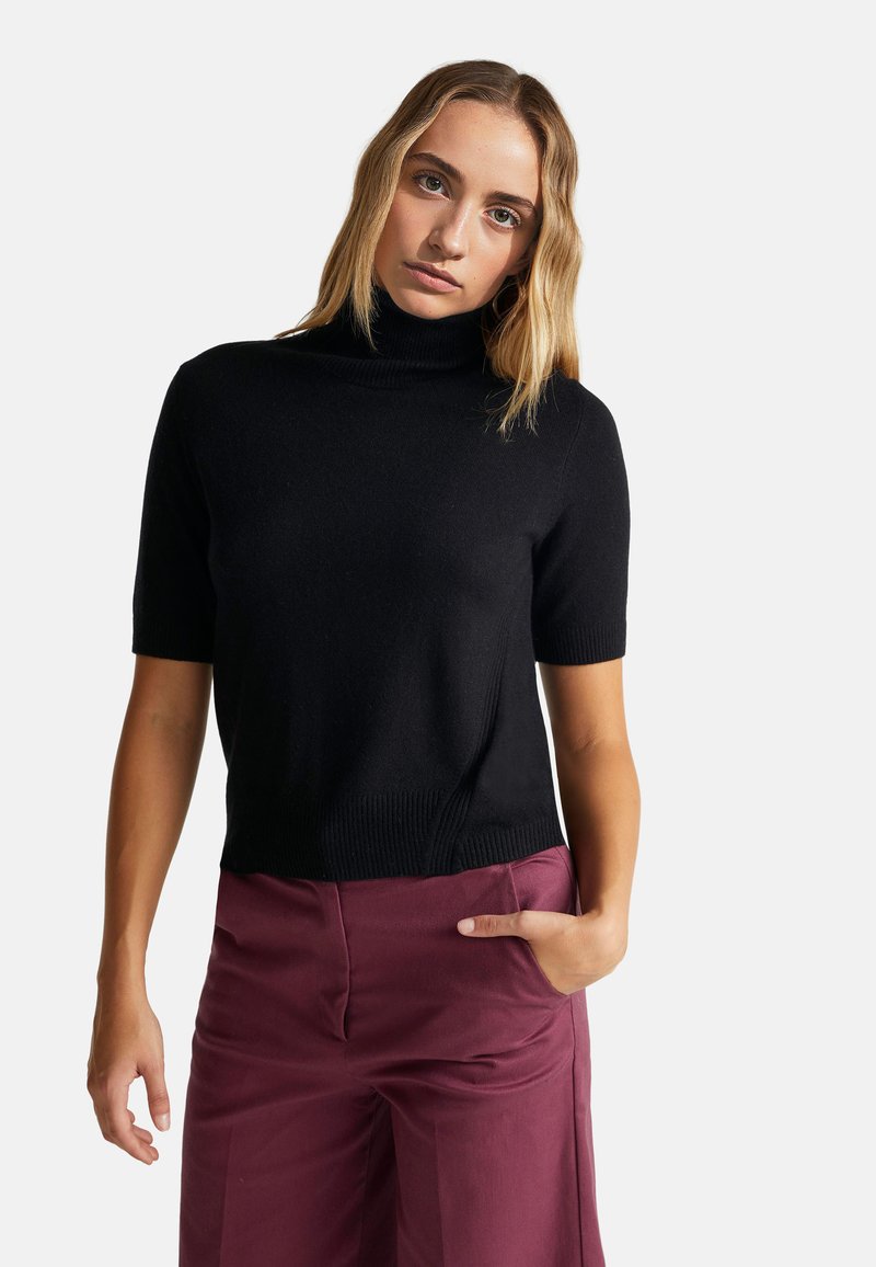 Černý krátký rukáv turtleneck svetr s jemnou texturou, s žebrovaným výstřihem a lemem, v kombinaci s vínovými kalhotami s vysokým pasem.