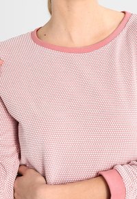 Camisa de manga larga rosa con un patrón texturizado de puntos y un cuello y puños acanalados en contraste. Tejido suave, diseño casual.
