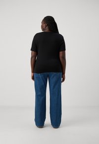 Top negro de manga corta combinado con pantalones de mezclilla de pierna ancha en azul claro. Textura suave con un diseño sencillo. Sin patrones o acentos destacables.