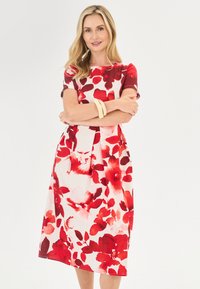 Blumenmusterkleid mit großen roten Blumen auf hellem Hintergrund, kurzen Ärmeln und knielanger Silhouette, aus einem weichen Stoff gefertigt.