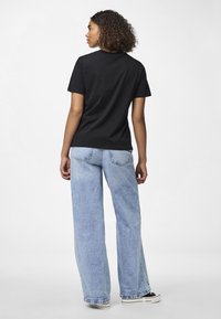 Juodas medvilninis marškinėlis su klasikinio kirpimo, dėvimas su šviesiai mėlynomis plačiomis kelnėmis. Apranga pasižymi atsitiktiniu stiliumi su minimaliais aksesuarais.