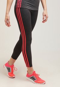 Leggings de sport noirs avec des rayures latérales rouges, accompagnés de chaussures de course roses vives avec des accents noirs et un revêtement en maille.