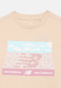 Camiseta beige con un gráfico colorido de un estadio lleno bajo un cielo azul y logotipos de New Balance debajo de la imagen.