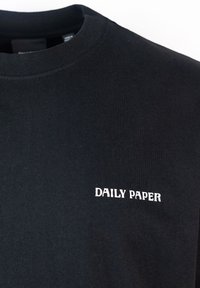 T-shirt in cotone nero con collo tondo, con testo ricamato bianco "DAILY PAPER" nella zona sinistra del petto. Tessuto semplice e texture.