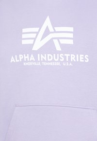 Svetlofialová mikina s bielym logom, ktoré obsahuje emblém a text "ALPHA INDUSTRIES" a "KNOXVILLE, TENNESSEE, U.S.A." na prednej strane.