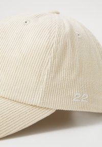 Beige corduroy cap with vertical ribbing, curved brim, embroidered '22' on the side, and small ventilation holes on the crown.