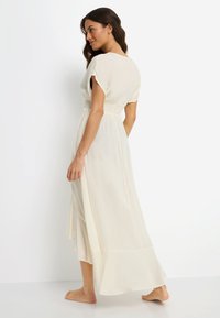 Κρεμ μακρύ φόρεμα με κοντά μανίκια, ελαστική μέση και αέρινη φούστα. Ελαφρύ ύφασμα με απαλή υφή και στρογγυλεμένο τελείωμα.