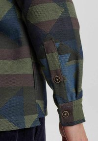 Camicia con bottoni realizzata in un tessuto testurizzato con motivi geometrici nei toni di blu, verde e marrone. Maniche con polsini e bottoni marroni.