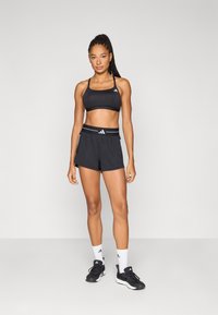 Black sports bra and matching shorts, made of lightweight fabric. Features white accents, elastic waistband, and plain design. Black shoes and white socks.