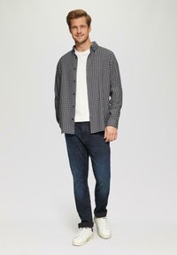Gekruiste knopshirt in zwart en wit over een wit t-shirt, gecombineerd met donkerblauwe jeans en witte sneakers. Casual outfit.