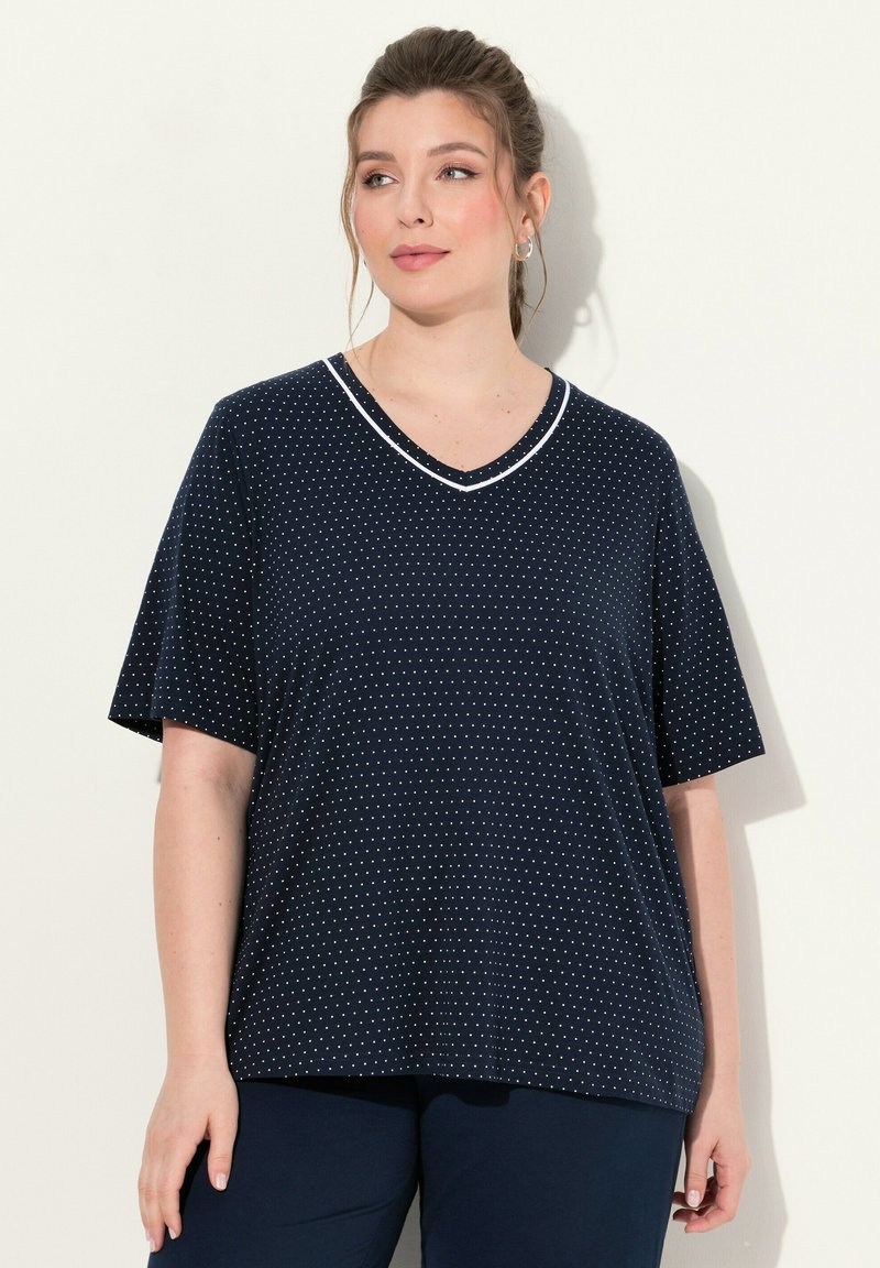 Námorně modré tričko s V-výstřihem, které má bílé puntíky, krátké rukávy a kontrastní bílý lem kolem výstřihu. Měkká tkanina.