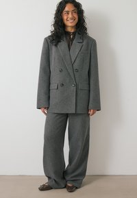Siv taksni blazer z dvojno zapenjanje in široke hlače iz teksturirane tkanine. Blazer ima ovratnik z zarezami in gumbnima žepoma.
