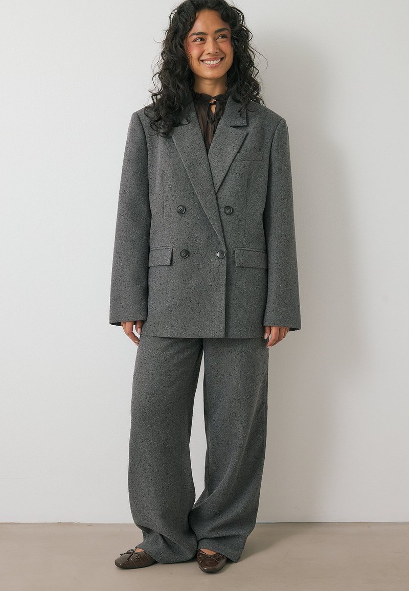 Siv taksni blazer z dvojno zapenjanje in široke hlače iz teksturirane tkanine. Blazer ima ovratnik z zarezami in gumbnima žepoma.
