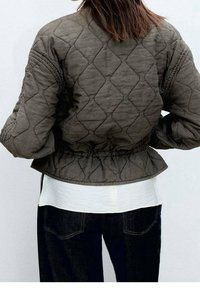 Quilted bomberjakke i olivengrøn, med en tætsiddende elastisk talje og tekstureret mønster, med en hvid lagdelt top under.