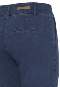 Jean en denim bleu marine montrant la vue arrière avec poche arrière et passants de ceinture, avec une petite étiquette de marque en cuir marron sur la ceinture.