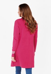 Cardigan lungo rosa con una texture liscia, caratterizzato da strisce bianche sui polsini, vestibilità su misura e sottili spacchi laterali per facilitare i movimenti.