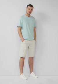 Jasnoniebieska koszulka z krótkim rękawem w połączeniu z beżowymi szortami do kolan i białymi trampkami, cechująca się luźnym krojem i prostym designem.