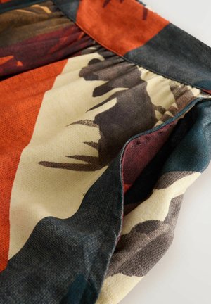 Tygkjol med ett färgglatt abstrakt mönster i orange, beige, svart och teal. Har en rynkad midja och en lätt textur.