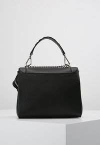 Sac à main en cuir noir avec une surface texturée, doté d'une anse supérieure et d'une accent en chaîne argentée le long du bord supérieur.