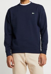 Sudadera azul marino de algodón. Presenta un cuello redondo, puños acanalados y un pequeño logo verde en el pecho. Corte clásico.