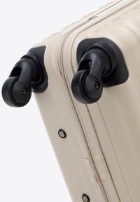 Nahaufnahme einer beigen Hartschalen-Kofferecke mit zwei schwarzen Spinner-Rädern und Reißverschlussverschluss.