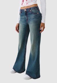 Dzwony z niebieskiego denimu, z efektem sprania, różowym przeszyciem i pięcioma kieszeniami. Połączone z białymi trampkami.