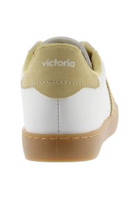 Vit sneaker med beige mocka hälla märkt "victoria" och sula av gummirubber, visad bakifrån.