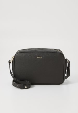 Sacoche en cuir noir à bandoulière avec finition texturée, fermeture éclair, sangle ajustable et logo métallique sur le devant.