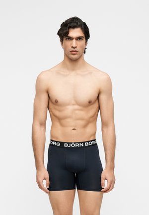 Άνδρας χωρίς πουκάμισο, στέκεται μπροστά φοράει μαύρα μποξεράκια Björn Borg μπροστά σε απλό λευκό φόντο.