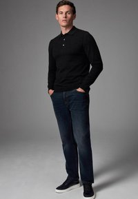 Sort langærmet polo med krave, parret med mørkeblå jeans og sorte sneakers, med en glat tekstur og slim fit.