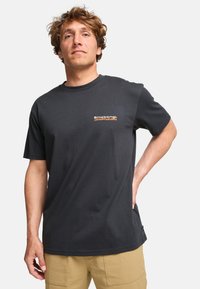 Musta puuvillainen t-paita lyhyillä hihoilla, pyöreällä kaula-aukolla ja pienellä oranssilla logolla rinnassa. Silkkinen rakenne ja rento fit.