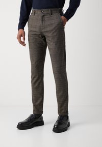 Nohavice z hnedého károvaného materiálu, slim fit so zapínaním v páse, prednými vreckami a gombíkovým zapínaním. Nosené s čiernymi mokasínami.