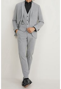 Jasnoszary garnitur składający się z marynarki, kamizelki i prostych spodni. Czarna koszula i czarne buty eleganckie dopełniają całość.